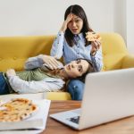 Par de amgas viendo una película en su laptop mientras comen pizza