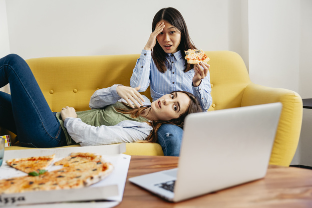 Par de amgas viendo una película en su laptop mientras comen pizza