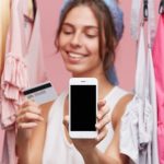 Mujer feliz con celular en la mano y tarjeta comprando ropa